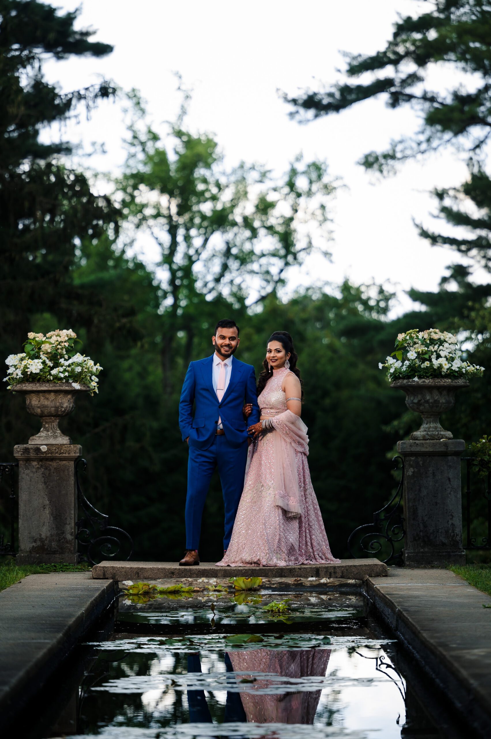Indian bride and groom pose in elegant attire in front of Skylands Manor in New Jersey.